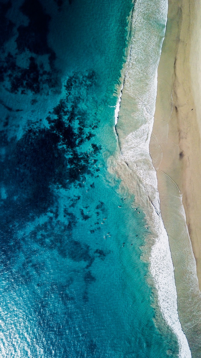 Aerial view of surfers in turquoise ocean waves near a sandy beach