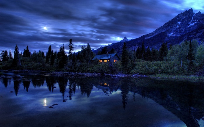 Cabin by a lake at night with mountains
