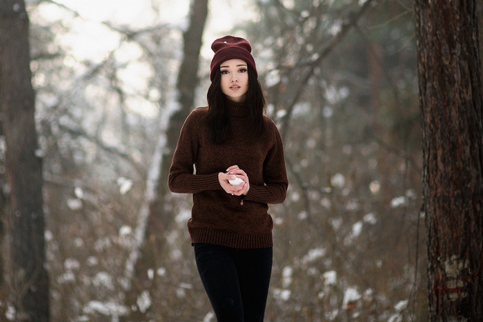 Woman in a maroon beanie and sweater holding a snowball in a snowy forest