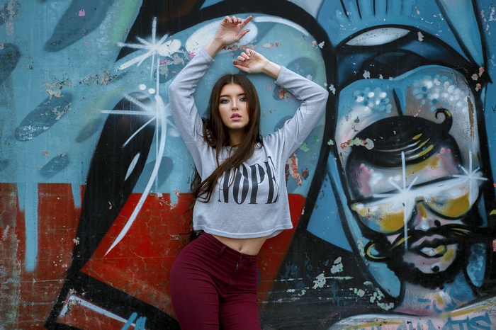 Woman in crop top and pants posing against graffiti wall