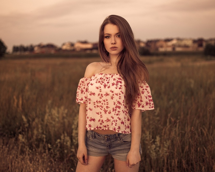 Woman with long hair wearing a floral off-the-shoulder top and jean shorts