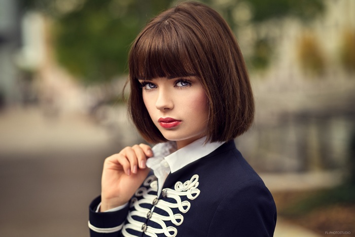 Woman with brown bob and bangs in a military-style jacket