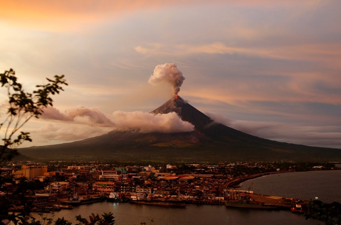 Volcano eruption over a coastal city at sunset