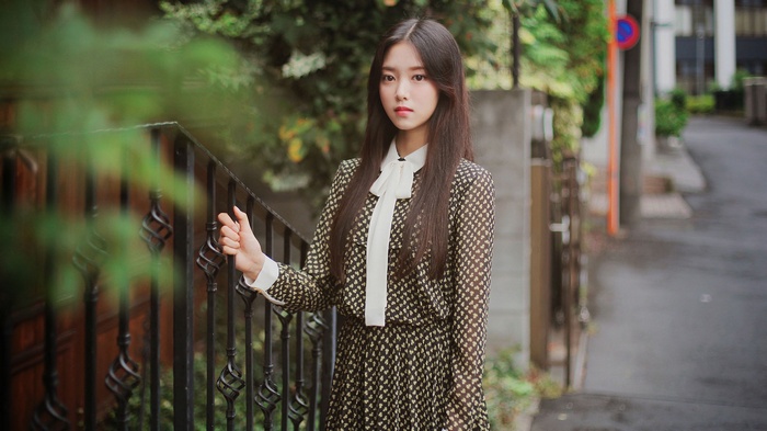 Woman in patterned dress with white bow standing by a fence