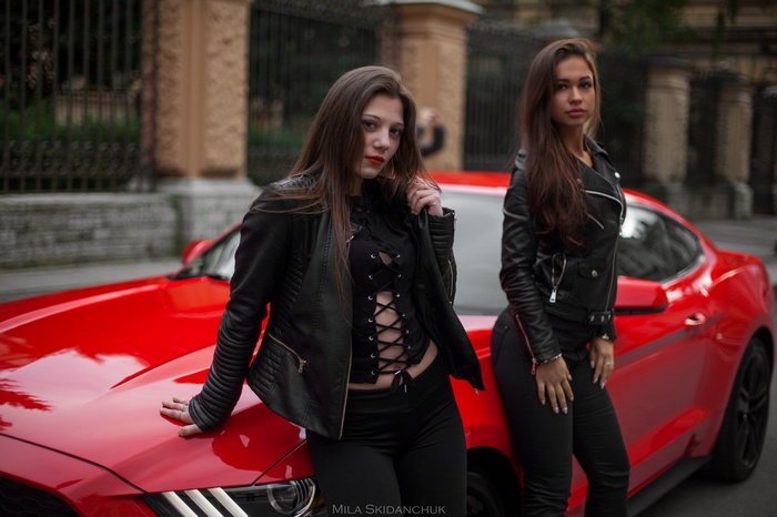 Two women in leather jackets with a red Ford Mustang