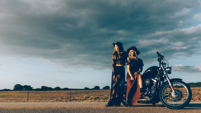 Two women in hats with a motorcycle on a road