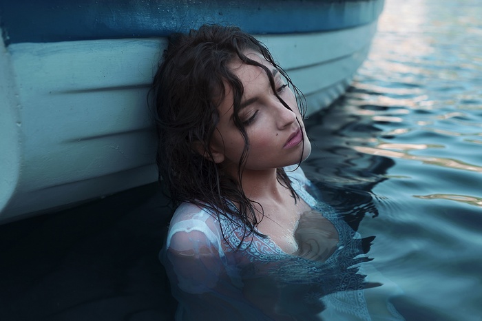Woman in white dress in water next to boat