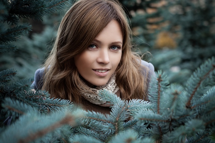 Woman with blue eyes peeking through pine branches