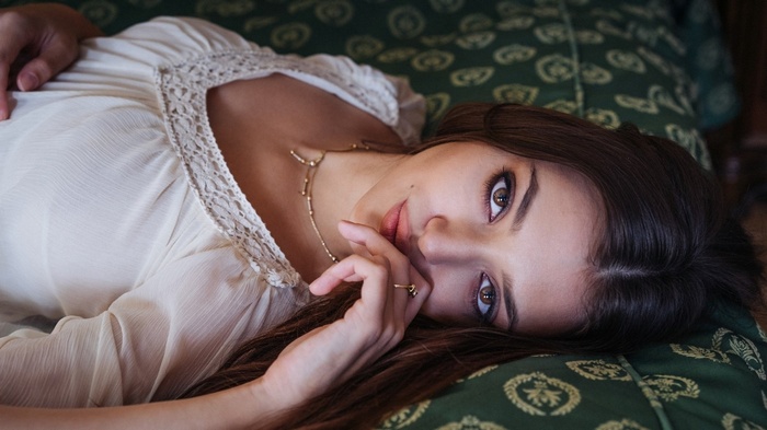 Woman with finger on lips lying on green fabric