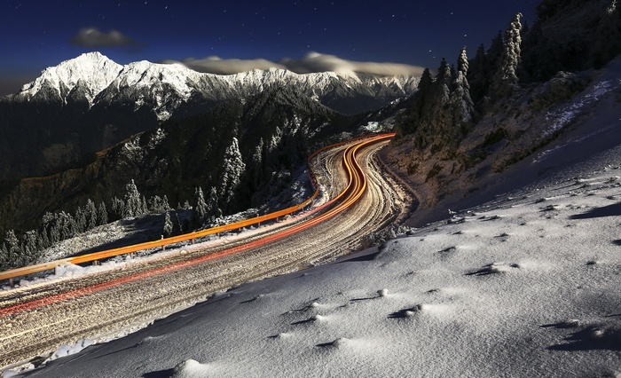 Snowy mountain road with car light trails at night