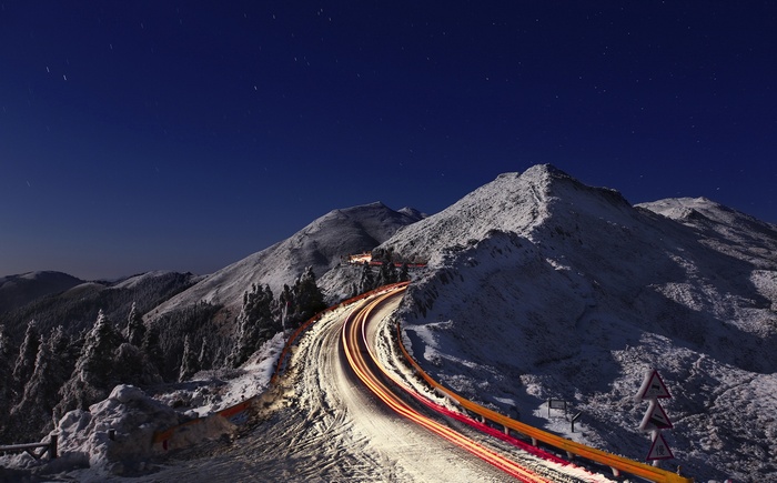 Snowy mountain road at night with light trails