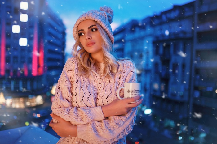 Woman in sweater and hat holding a mug in the snow