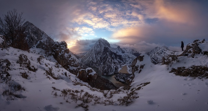 Snowy mountains with a person overlooking a valley at sunset