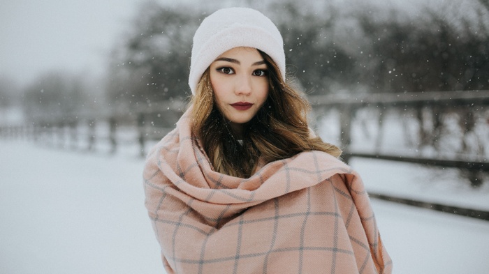 Woman in snow wearing a white hat and pink scarf
