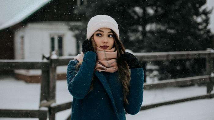 Woman in a blue coat and white hat in the snow