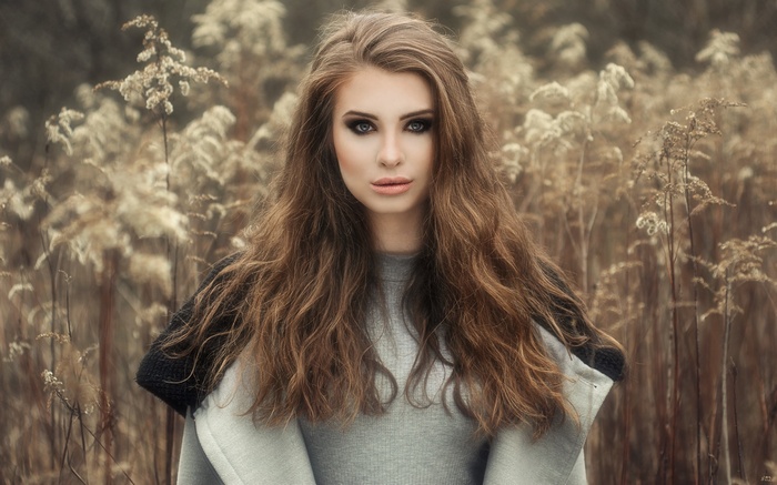 Woman with long brown hair and smoky eyes in a field