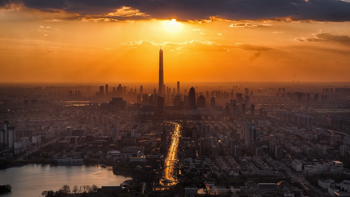 Cityscape at sunset with a tall skyscraper and a lake