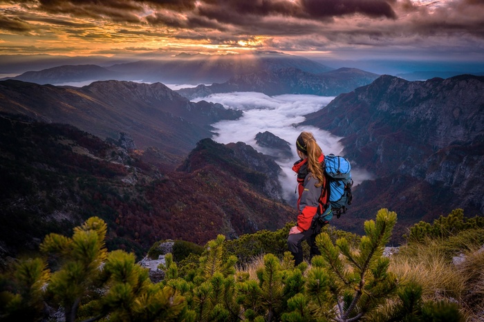 Woman with backpack on mountain overlooking misty valley at sunrise