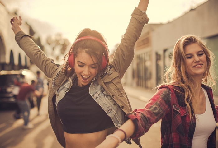 Two young women dancing with headphones on a street