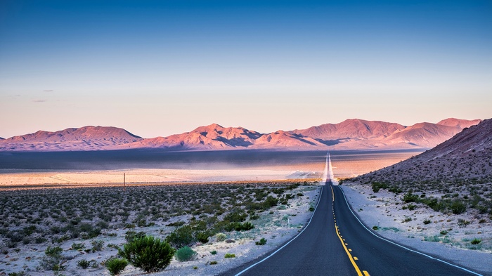 Desert road leading to mountains at sunset