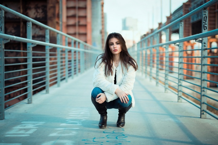 Woman in white jacket and jeans kneeling on a bridge