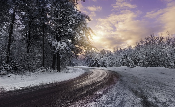 Winding snowy road through a winter forest at sunset