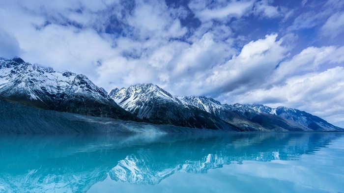 Snow-capped mountains reflected in a blue lake under a cloudy sky