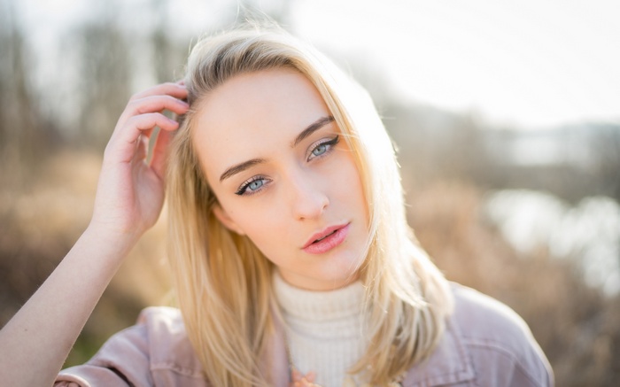 Woman with blonde hair and blue eyes touching her hair