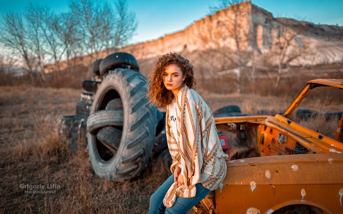 Woman with curly hair sitting near old tires and car