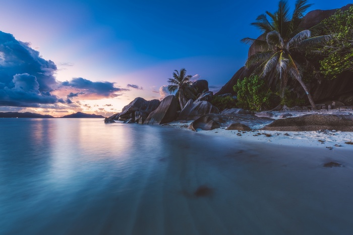 Sunset over the ocean with granite boulders and palm trees on La Digue, Seychelles