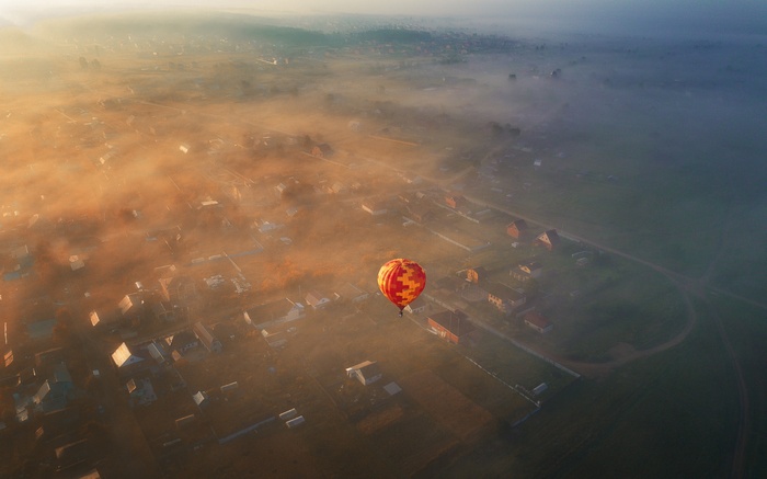 Hot air balloon over a foggy village at sunrise