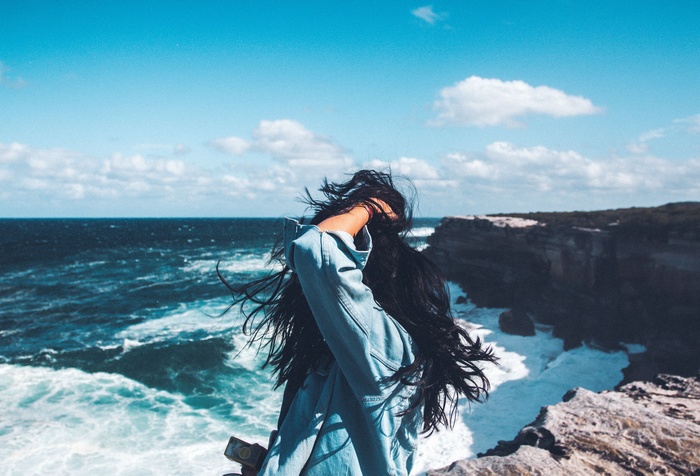 Woman with hands in hair on a cliff overlooking the sea