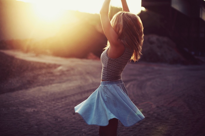 Woman in blue skirt with arms up at sunset