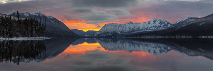 Snowy mountains and trees reflected in a lake at sunset