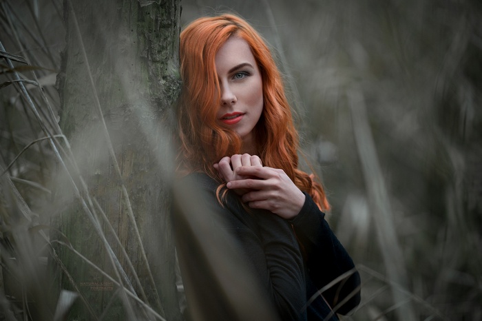 Woman with red hair leaning against a tree