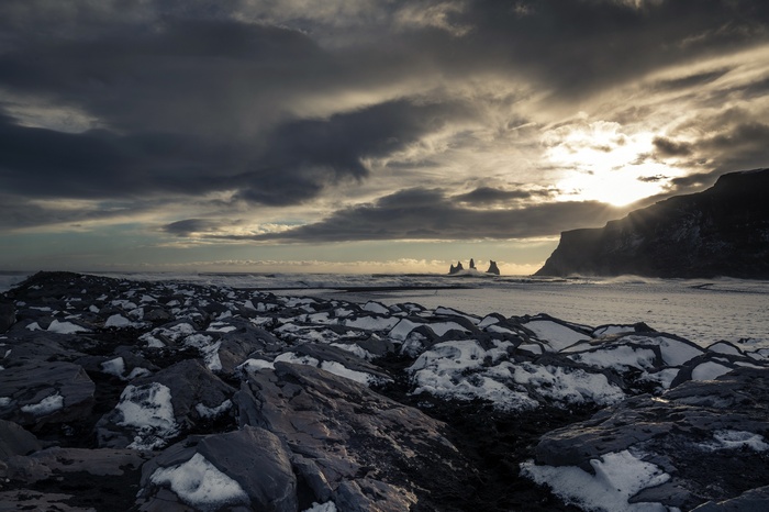 Rocky beach with snow and sea stacks at sunset