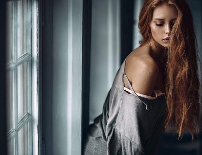 Woman with long red hair by a window