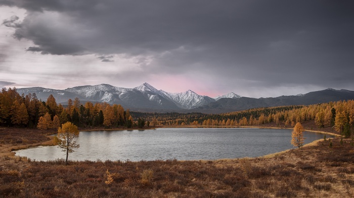 Autumn lake with snow-capped mountains and dark clouds