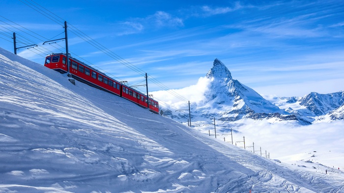 Red train ascending a snowy slope towards the Matterhorn in the Alps