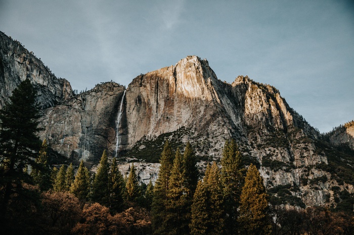 Waterfall cascading down a rocky mountain face with pine trees