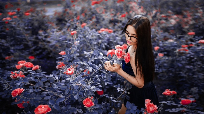 Woman in glasses smelling red roses in a garden