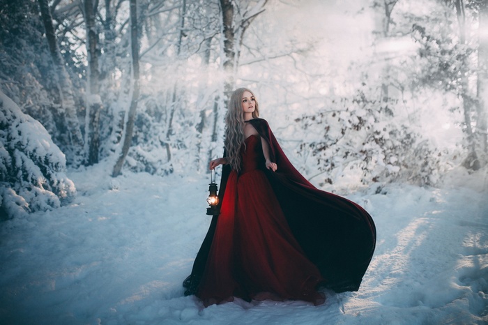 Woman in red dress holding lantern in snowy forest