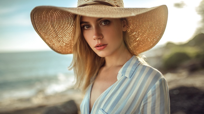 Ksenia Kokoreva wearing a straw hat and striped shirt by the sea