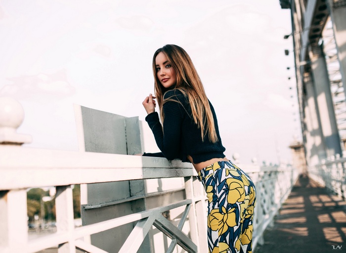 Woman in patterned pants leaning on a bridge railing