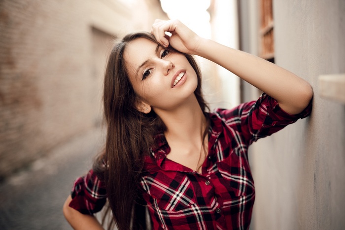 Woman in red plaid shirt leaning against a wall