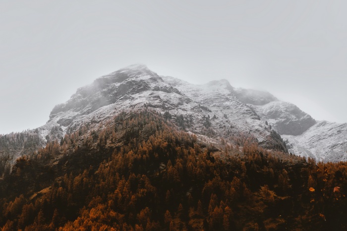 Snow-capped mountains with autumn trees under cloudy sky
