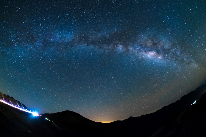 Starry night sky over mountains with car lights