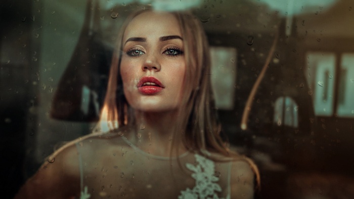 Woman with red lipstick and gray eyes behind water on glass