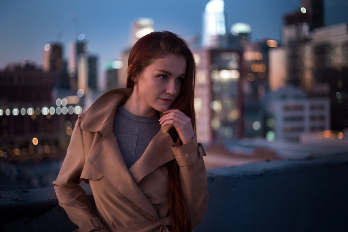 Emily Bloom in a trench coat with city skyline at dusk