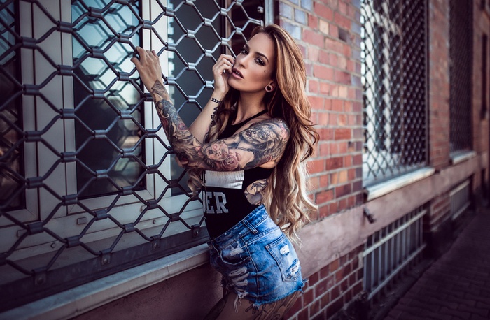 Tattooed woman in denim shorts by brick wall